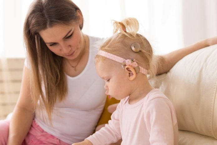 foto de uma mae branca sentada no sofa olhando para filha que parece estar mexendo num livro